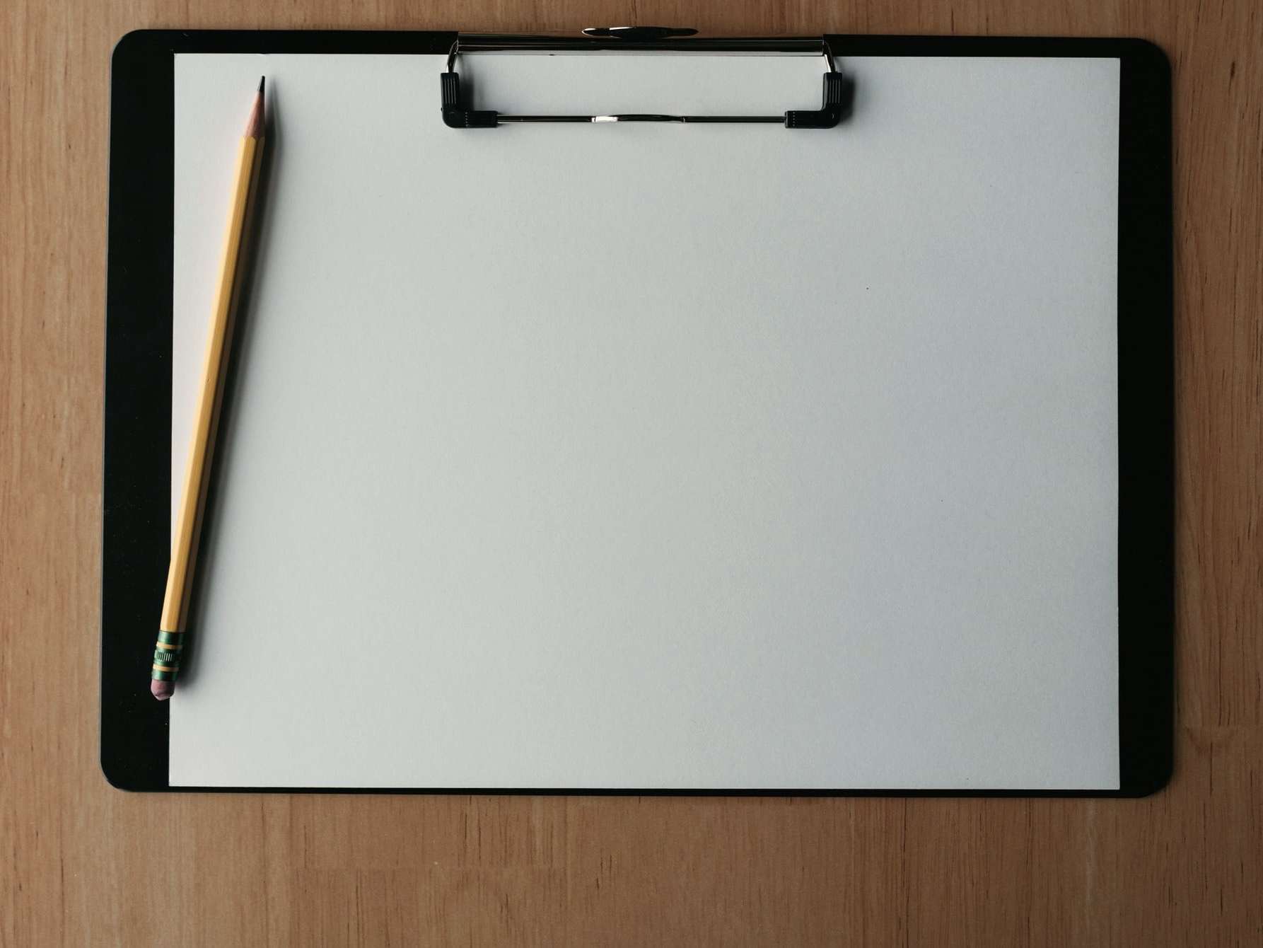Clipboard cu o foaie albă și un creion, pe o masă de lemn